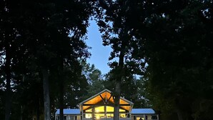Una cabaña de dos pisos con una chimenea central destacada, rodeada de un bosque denso.