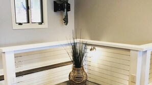 Un rincón de una habitación con suelo de madera, un banco blanco, una lámpara de pared y un jarrón decorativo con plantas altas.