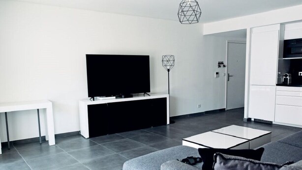 A modern living room with a grey sofa, a flat-screen TV, a white coffee table, and a pendant light. - APARTEMENT CANNES CROISETTE 4th floor (CANNES)