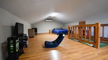 Ein Zimmer mit schrägem Dach, einem Fernseher, einem hölzernen Spielbereich und einem Sitzsack.