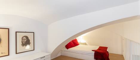 Un dormitorio con una cama blanca, almohadas rojas, un tocador blanco y piso de madera.