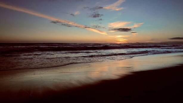 Uma praia ao pôr do sol, com ondas se aproximando da costa.