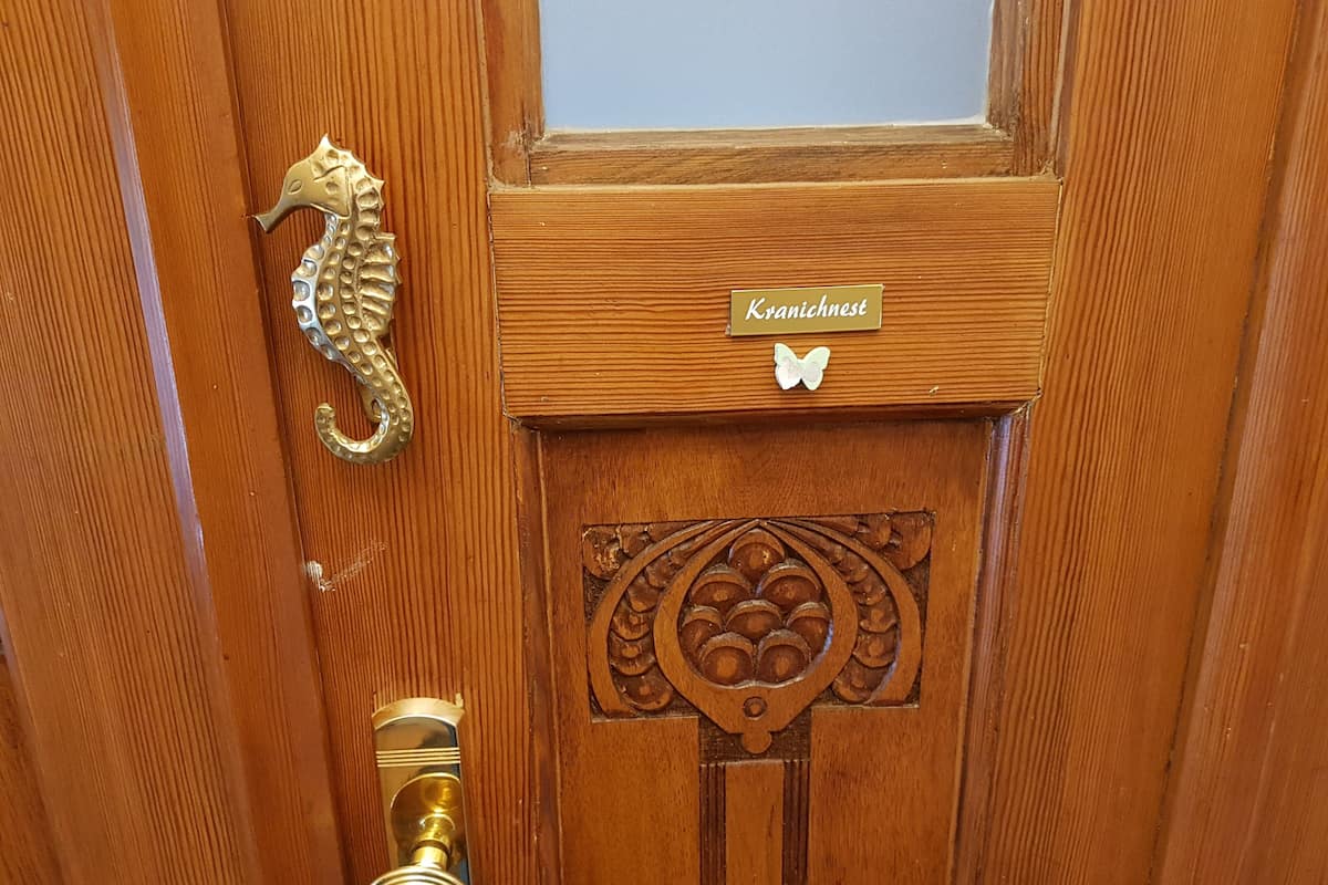 A wooden door with a brass knocker, a nameplate reading "Kranichnest," and a decorative panel.