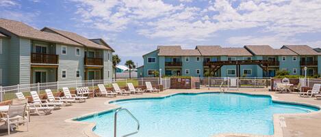 A swimming pool surrounded by lounge chairs and a building with multiple balconies.