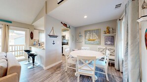 A cozy dining area with a round table and white chairs, a kitchen with white cabinets, and nautical-themed decorations. - 2nd Floor, Pet Friendly, Close to Marina and Ferry, Golf Cart Access (Port Aransas)