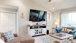 A living room with a flat-screen TV mounted on the wall, a white cabinet with glass doors, a blue sofa, and a coffee table. - 2nd Floor, Pet Friendly, Close to Marina and Ferry, Golf Cart Access (Port Aransas)