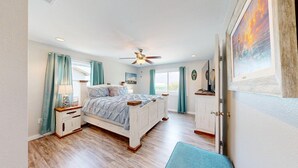 A bedroom with a bed, a ceiling fan, a nightstand, a dresser, and a window with curtains. - 2nd Floor, Pet Friendly, Close to Marina and Ferry, Golf Cart Access (Port Aransas)