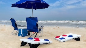 Montaje de playa con una sombrilla azul, dos sillas de playa, un enfriador y dos tableros blancos con pelotas de colores.
