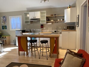 Une cuisine moderne avec un îlot central, des tabourets de bar, une table à manger et un canapé rouge.