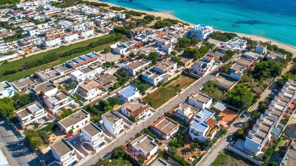 An aerial view of a coastal residential area with houses arranged in rows along a street, adjacent to a beach. - Villa Stella Blu by BarbarHouse (San Pietro in Bevagna)