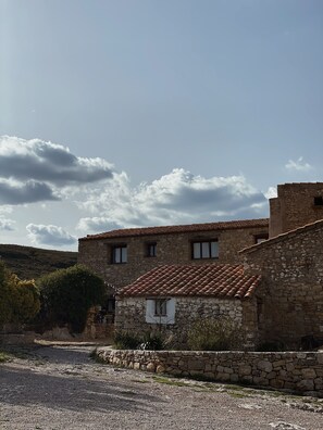A stone building with a tiled roof, a small window, and a stone wall in front. - Charming Rural House with Pool, 34 km from the Mediterranean (Catí)