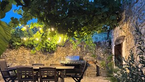 Un patio in pietra con una griglia, un tavolo da pranzo e sedie, circondato da vasi di piante e un muro di pietra.