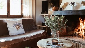 Un accogliente soggiorno con camino, un divano con un cuscino decorativo, un tavolino con un vaso e una candela, e un televisore su uno scaffale.