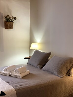 A neatly made bed with pillows and folded towels, a bedside lamp, and a woven basket with flowers on the wall. - Charming Rural House with Pool, 34 km from the Mediterranean (Catí)
