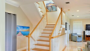 Un escalier avec des rampes en bois menant à l’étage supérieur, un tableau accroché au mur, une chaise et un téléviseur posé sur un meuble.
