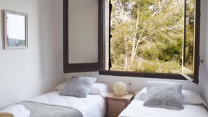 Een slaapkamer met twee bedden, een nachtkastje, een spiegel en een raam met uitzicht op bomen.