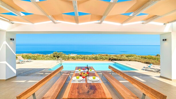 A dining area with a table set for four, overlooking a pool and the sea. - Vista Mare Maxima Heated Pool (Georgioupoli)