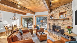 A cozy living room with leather sofas, a stone fireplace, and a dining area with wooden furniture.