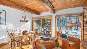 A cozy interior with a wooden ceiling, large windows, a dining area, and a leather sofa.