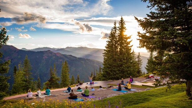 A group of people practicing yoga on a grassy slope with a mountain view in the background.