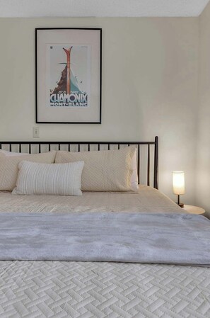 Un lit recouvert d’une courtepointe matelassée, un tableau encadré accroché au mur et une lampe de chevet.