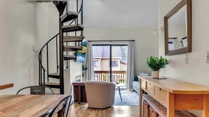 A modern interior with a spiral staircase, a dining area, a large window with a view, and a wooden bench. - SnowPine Condo, Sleeps 6, King Bed, Patio (Ellicottville)