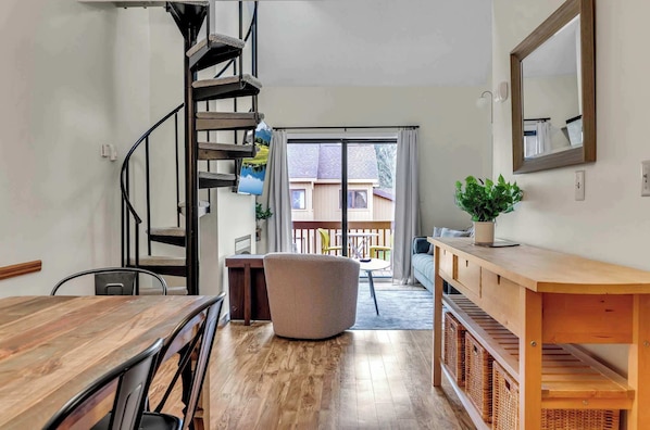A modern interior with a spiral staircase, a dining area, a large window with a view, and a wooden bench. - SnowPine Condo, Sleeps 6, King Bed, Patio (Ellicottville)