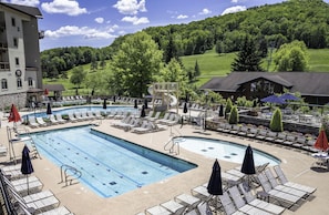 A pool area with lounge chairs, a water slide, and a view of a green landscape.