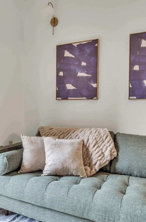 Une pièce avec un canapé vert, deux coussins et deux tableaux abstraits accrochés au mur.