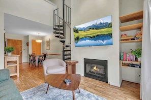 A living room with a fireplace, a TV mounted on the wall, a staircase, and a dining area.