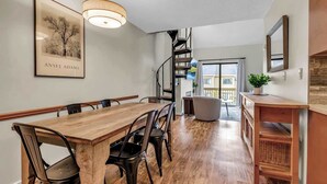 A dining area with a wooden table and chairs, a staircase, and a view to the outside. - SnowPine Condo, Sleeps 6, King Bed, Patio (Ellicottville)