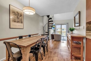 A dining area with a wooden table and chairs, a staircase, and a view to the outside. - SnowPine Condo, Sleeps 6, King Bed, Patio (Ellicottville)