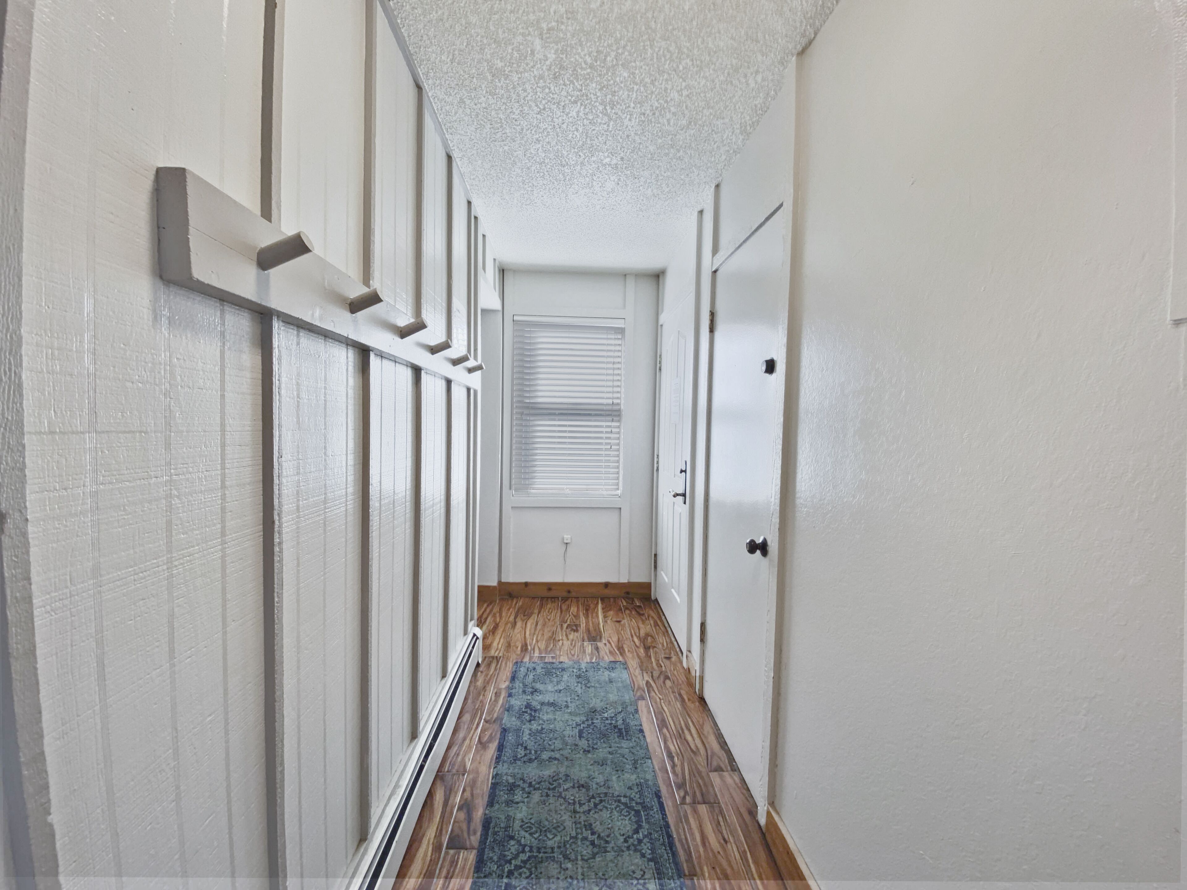 A narrow hallway with white walls, a wooden floor, and a blue patterned rug.