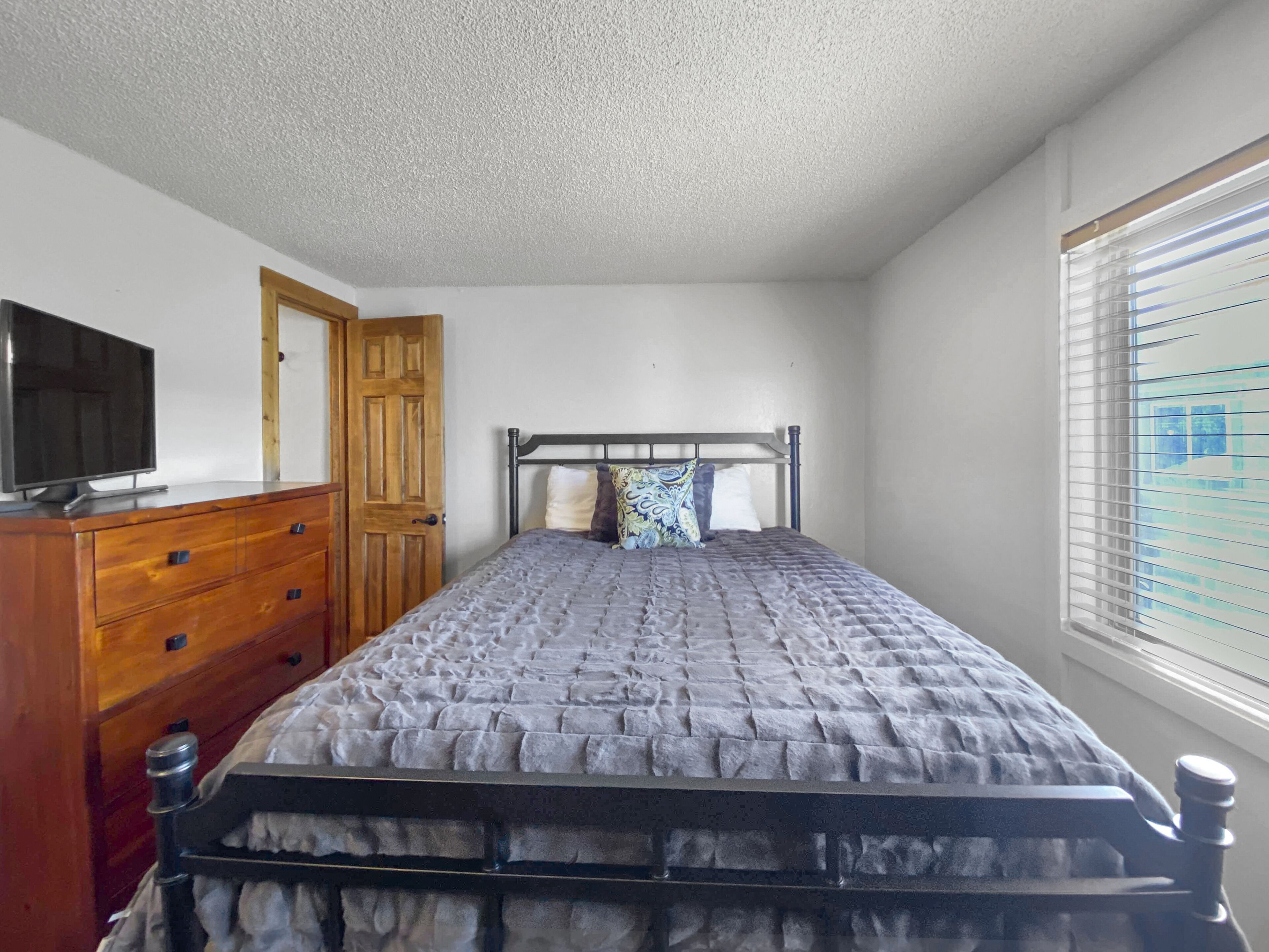 Une chambre à coucher avec un lit, une commode en bois et un téléviseur posé sur une autre commode.