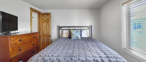 Une chambre à coucher avec un lit, une commode en bois et un téléviseur posé sur une autre commode.