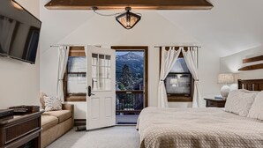 A bedroom with a large bed, a TV mounted on the wall, a wooden desk, and a view of mountains through an open door. - Newly Renovated! Downtown Breck, Private Hot Tub, 5 Fireplaces-Abbett Placer His (Breckenridge)