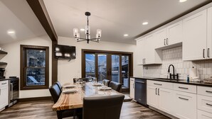 A modern kitchen with white cabinets, a wooden dining table, and a chandelier. - Newly Renovated! Downtown Breck, Private Hot Tub, 5 Fireplaces-Abbett Placer His (Breckenridge)