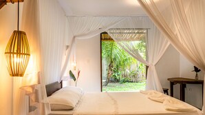 Une chambre avec un grand lit, des rideaux blancs et une vue sur un jardin tropical.