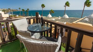 Een balkon met rieten meubilair, een tafel met een fles en uitzicht op zee en palmbomen.