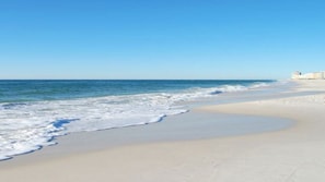 A beach with a clear sky, calm waves, and a distant building. - Spectacular Spacious 7th Floor Romar House with large deck to watch the waves. (Orange Beach)