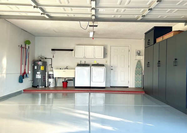 A clean, well-lit garage with a water heater, washing machine, and storage cabinets. - Prime Location: Single-Level Gem w/ Garage & Pool! (Chandler)