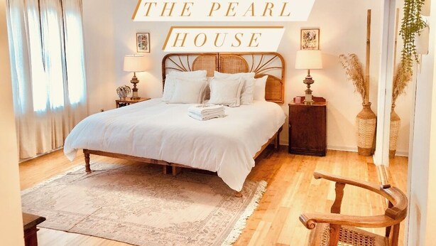 Una camera da letto curata con un letto grande, lampade sui comodini, uno specchio decorativo e un cartello con la scritta "THE PEARL HOUSE".