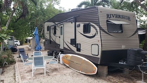 Een RV aan de rivier met een overdekte patio, inclusief buitenmeubels en een ventilator.