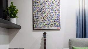 A living room with a grey sofa, a green pillow, a guitar, and a colorful abstract painting on the wall. - *Get-Away by River Trail, Hot Tub, Fire Pit, Bikes, Grill (Kerrville)