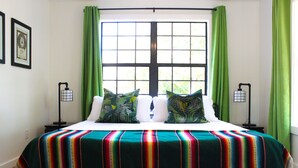 A bed with a colorful striped bedspread, two pillows, and green curtains. - *Get-Away by River Trail, Hot Tub, Fire Pit, Bikes, Grill (Kerrville)