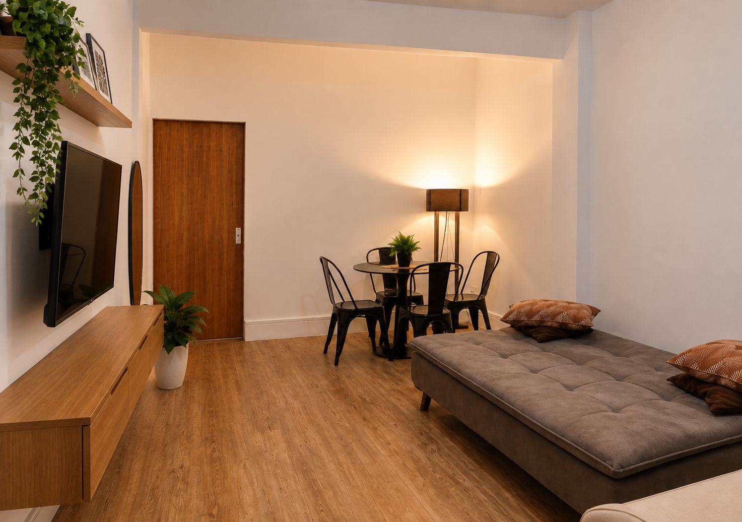 A compact living space with a sofa, a dining table with chairs, a TV mounted on the wall, and a door.