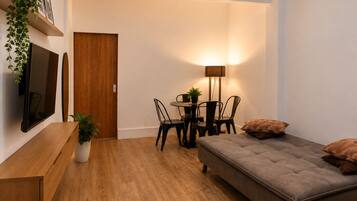 A compact living space with a sofa, a dining table with chairs, a TV mounted on the wall, and a door.