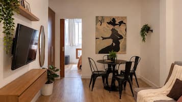 Una sala moderna con un televisor de pantalla plana, una zona de comedor con una mesa redonda y sillas, y un cuadro abstracto grande en la pared.