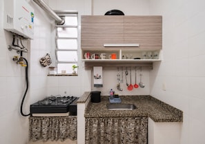 A compact kitchen with a gas stove, a sink, and a window with blinds. - Copacabana: quiet apartment near the beach and metro (RJ)
