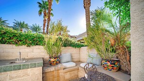 A patio with a built-in sink, a cushioned seating area, and a table. - Casa La Paz Getaway – Private Spa & BBQ,  Pool 2br (La Quinta)